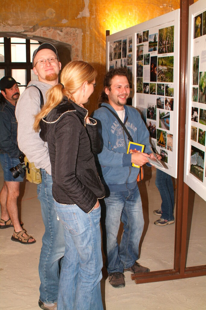 Návštěvníci si prohlížejí fotografie na výstavních panelech v klenuté místnosti